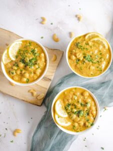 Chickpea curry in white bowls garnished with lemon slices and cilantro.