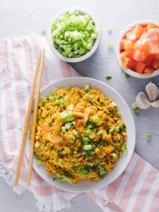 Scrambled tofu with vegetables and green onions in a white bowl on a gray surface.