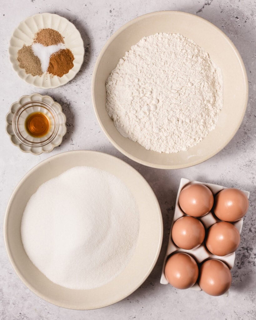 A clear image showing flour, eggs, spices, vanilla, and honey on a light surface, ready for baking.