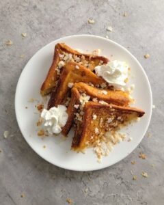 Golden French toast slices topped with whipped cream and chopped nuts on a white plate.