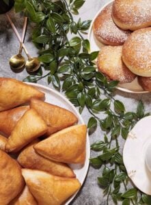 Golden fried samosas on a white plate with green decorative leaves.