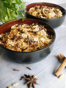 Savory rice dish topped with star anise and spices in black bowls on rustic table.