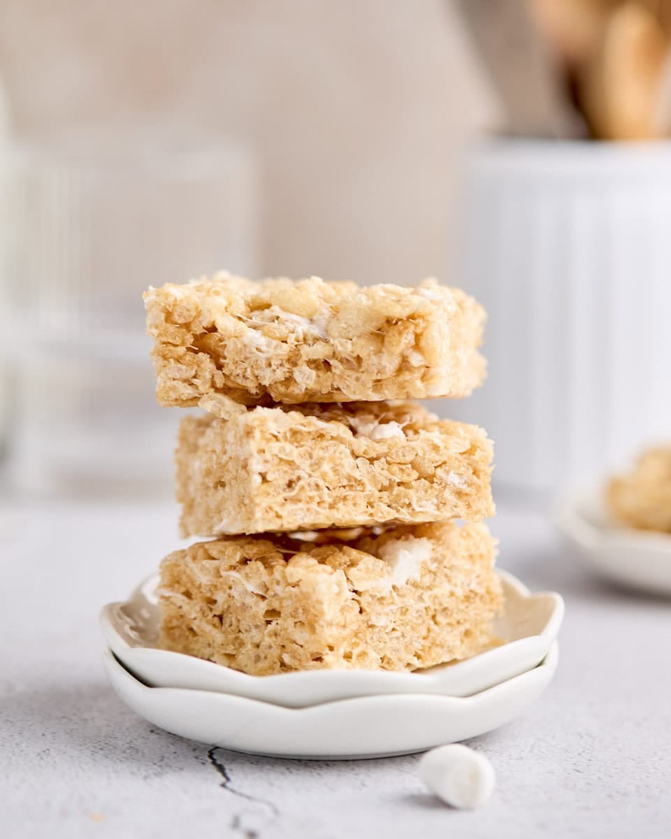 Soft, layered rice krispie treats stacked in a small dish, with a blurred background.