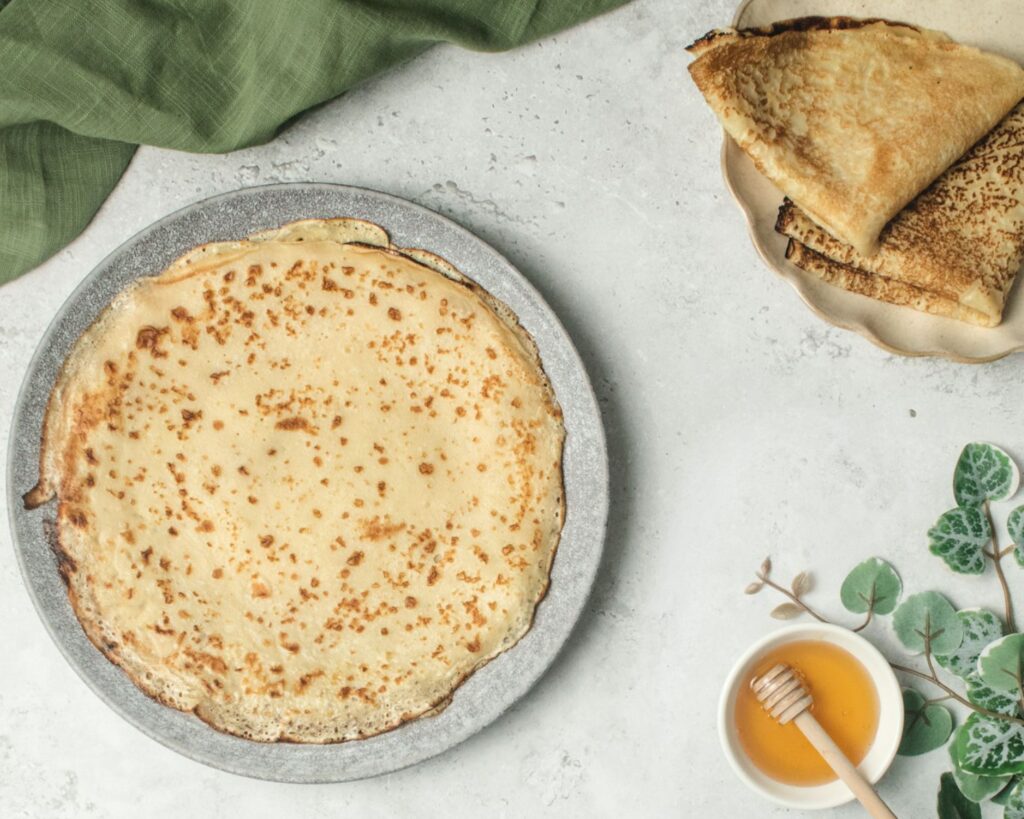 Crepes on a plate with honey and herbs in the background.