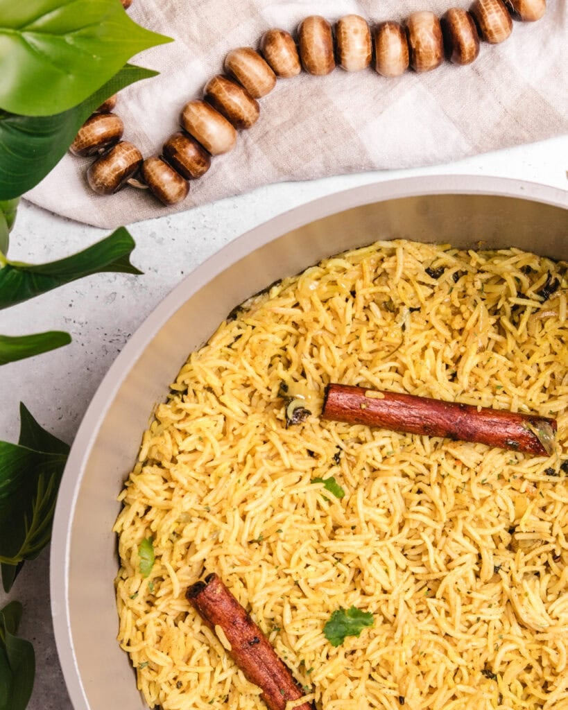 Close-up of yellow rice with cinnamon sticks and herbs in a white dish.