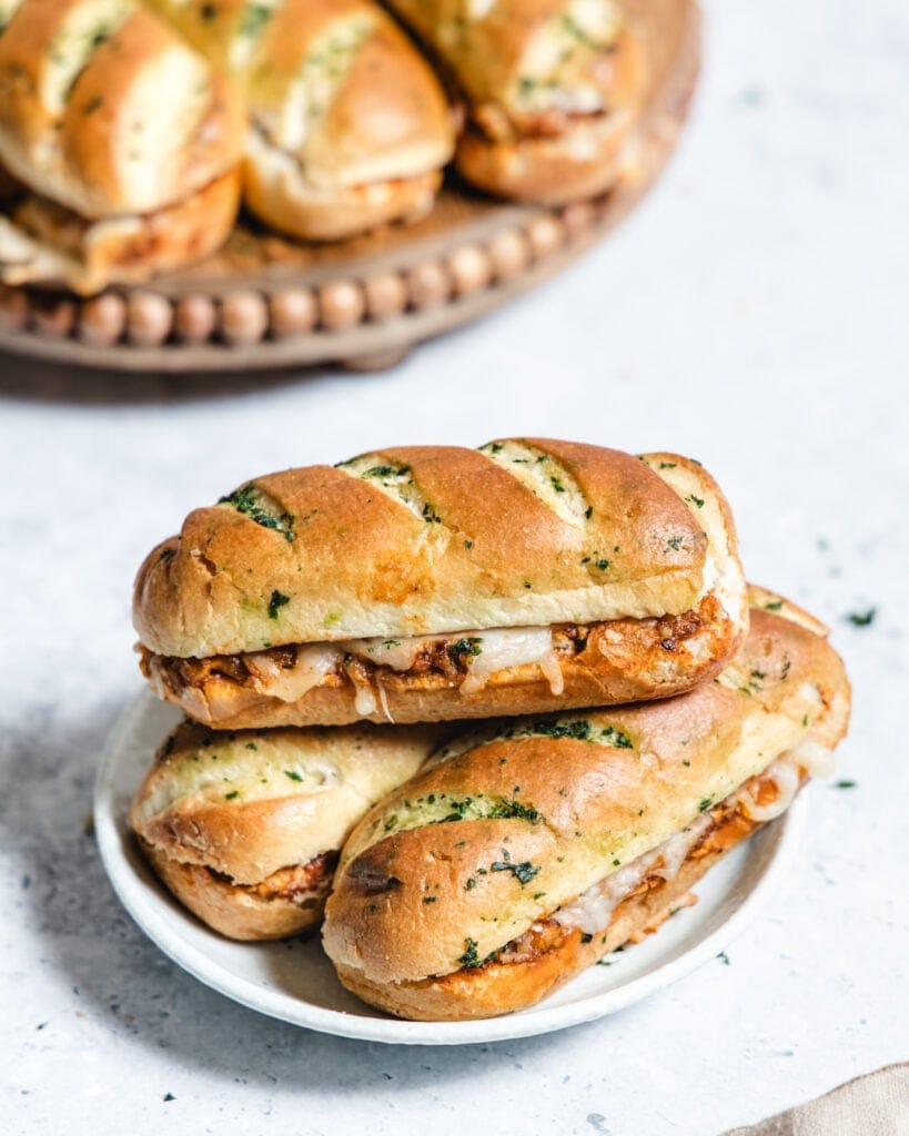 Three garlic herb baguette sandwiches with chicken and cheese on a white plate.