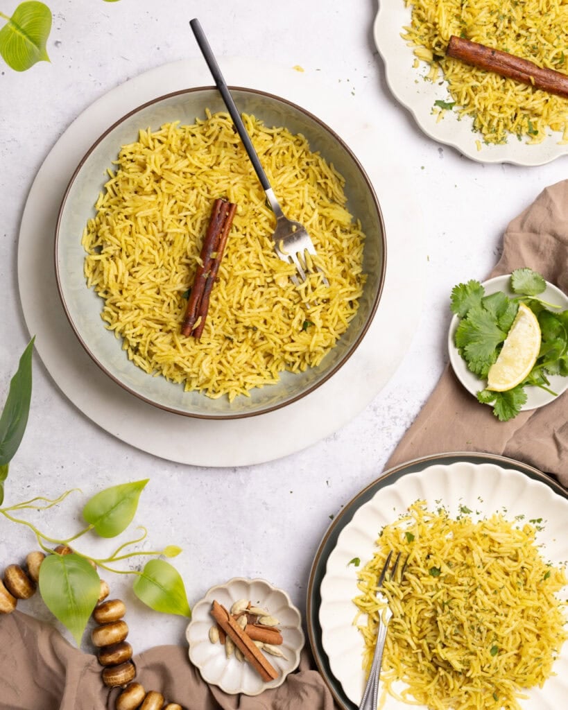 Yellow rice with cinnamon stick and lime wedge on a white plate.