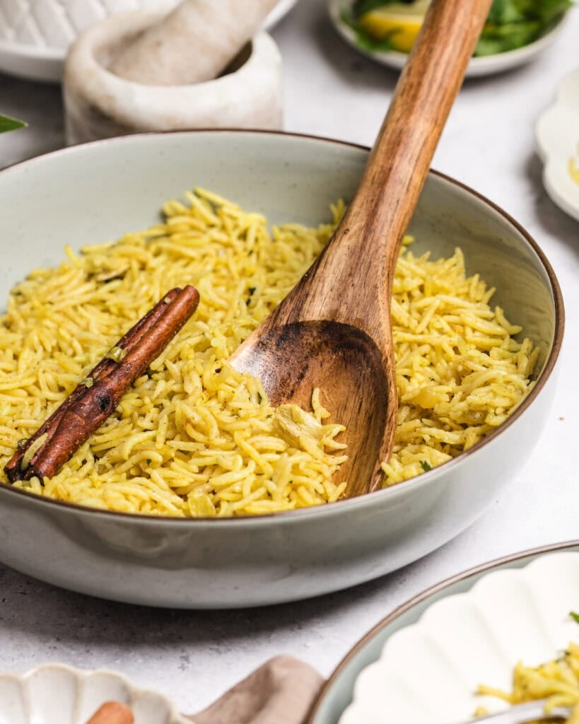 Bowl of yellow turmeric rice with a cinnamon stick and wooden spoon.
