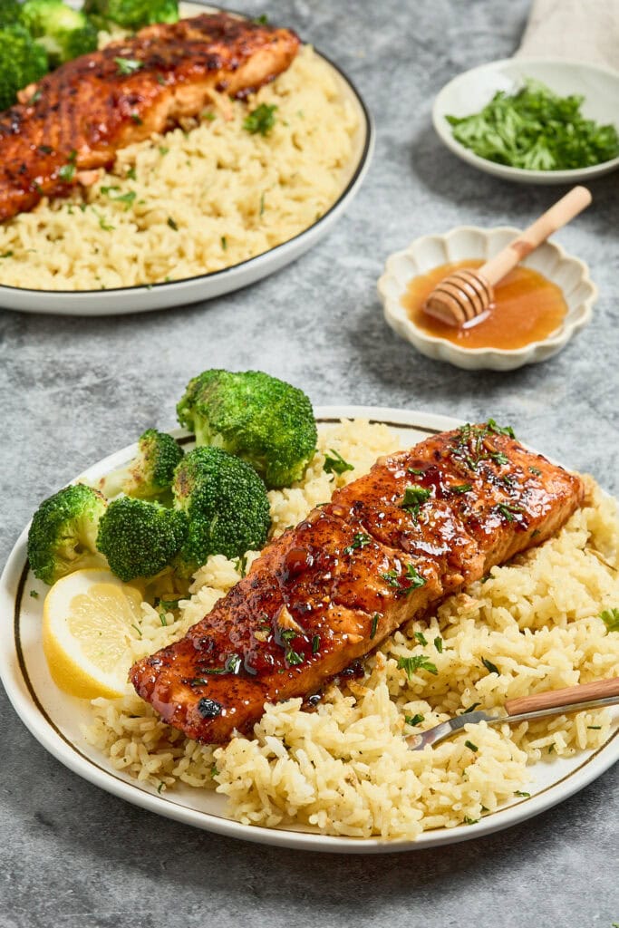 Grilled salmon fillet on rice with broccoli and lemon wedge.